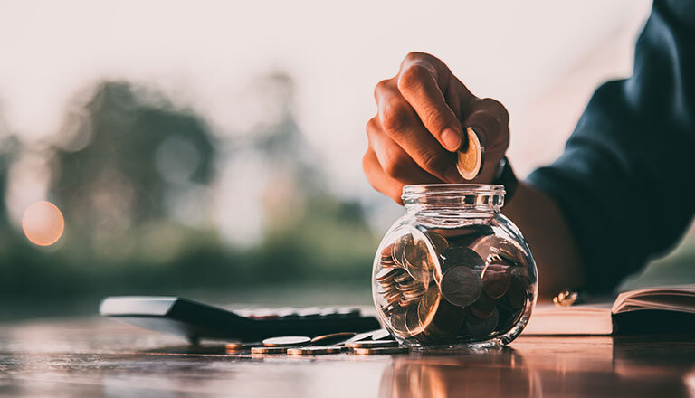 Finanzen: Eine Hand steckt Münzen in ein Gefäß