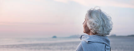 Header Rente retten Frau blickt auf das Meer im Sonnenuntergang