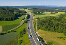 Autobahn führt durch Natur, grüne Wiesen, Windräder am Horizont, auf der Autobahn fahren Pkw und LKW. Text auf Bild: Mehr Tempo bei Straßen, mehr Marktwirtschaft beim Klimaschutz