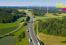 Autobahn führt durch Natur, grüne Wiesen, Windräder am Horizont, auf der Autobahn fahren Pkw und LKW. Text auf Bild: Mehr Tempo bei Straßen, mehr Marktwirtschaft beim Klimaschutz