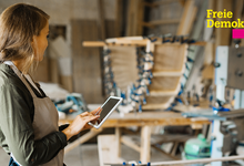 Selbstständige Handwerkerin steht in der Werkstatt mit einem iPad in der Hand