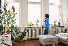Frau steht in Wohnung am Fenster vor zwei Heizkörpern