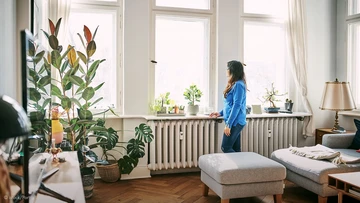 Frau steht in Wohnung am Fenster vor zwei Heizkörpern
